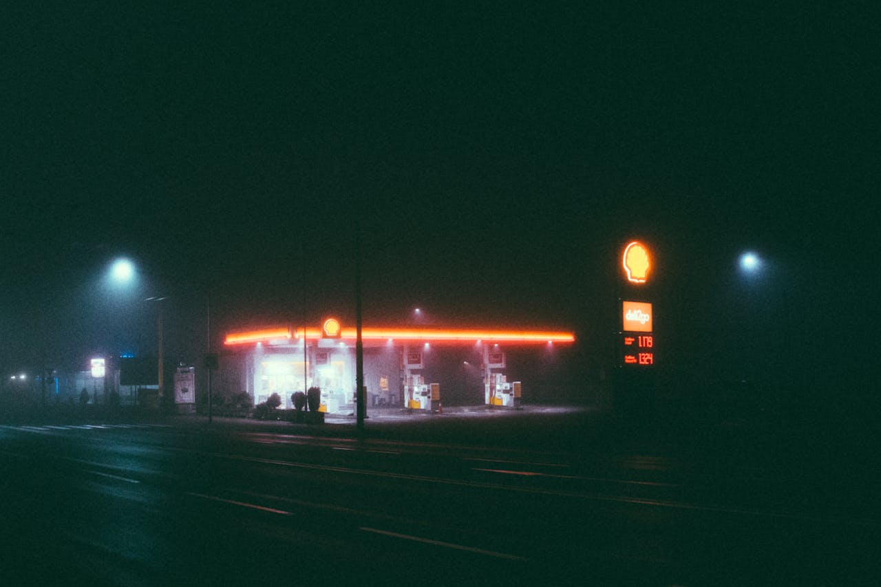 A foggy night scene of an illuminated gas station, featuring vibrant neon lights.